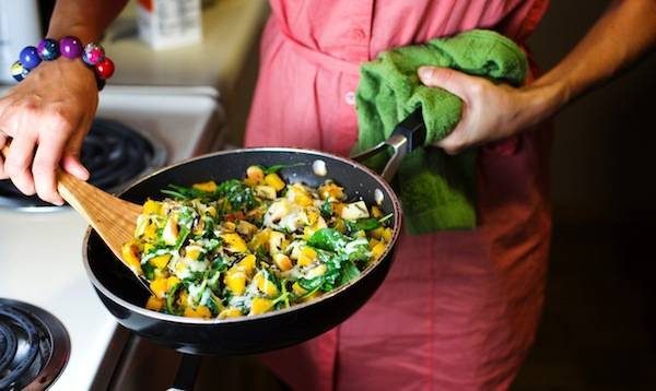 Woman holding a skillet with a wooden spoon.