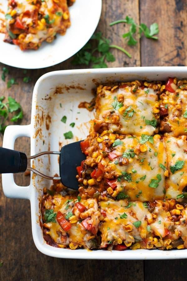 Mexican casserole being scooped out of a white pan with a spatula.