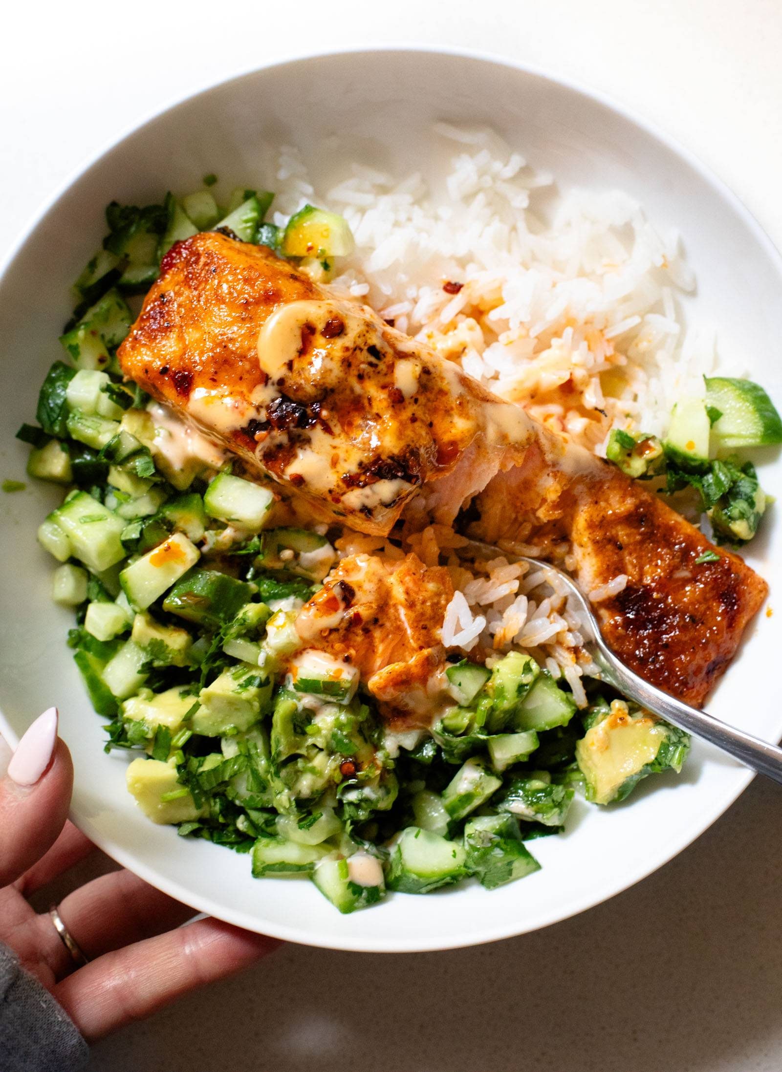 Bang bang salmon in a bowl with rice and cucumber salad.